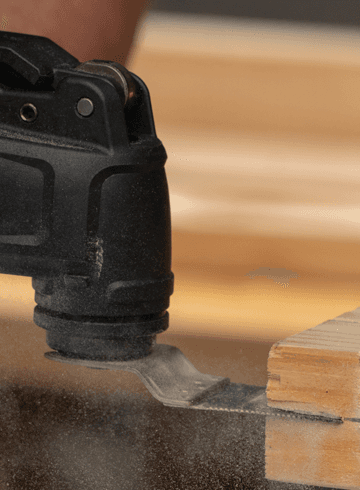 Oscillating multi-tool cutting into a wood block with sawdust flying