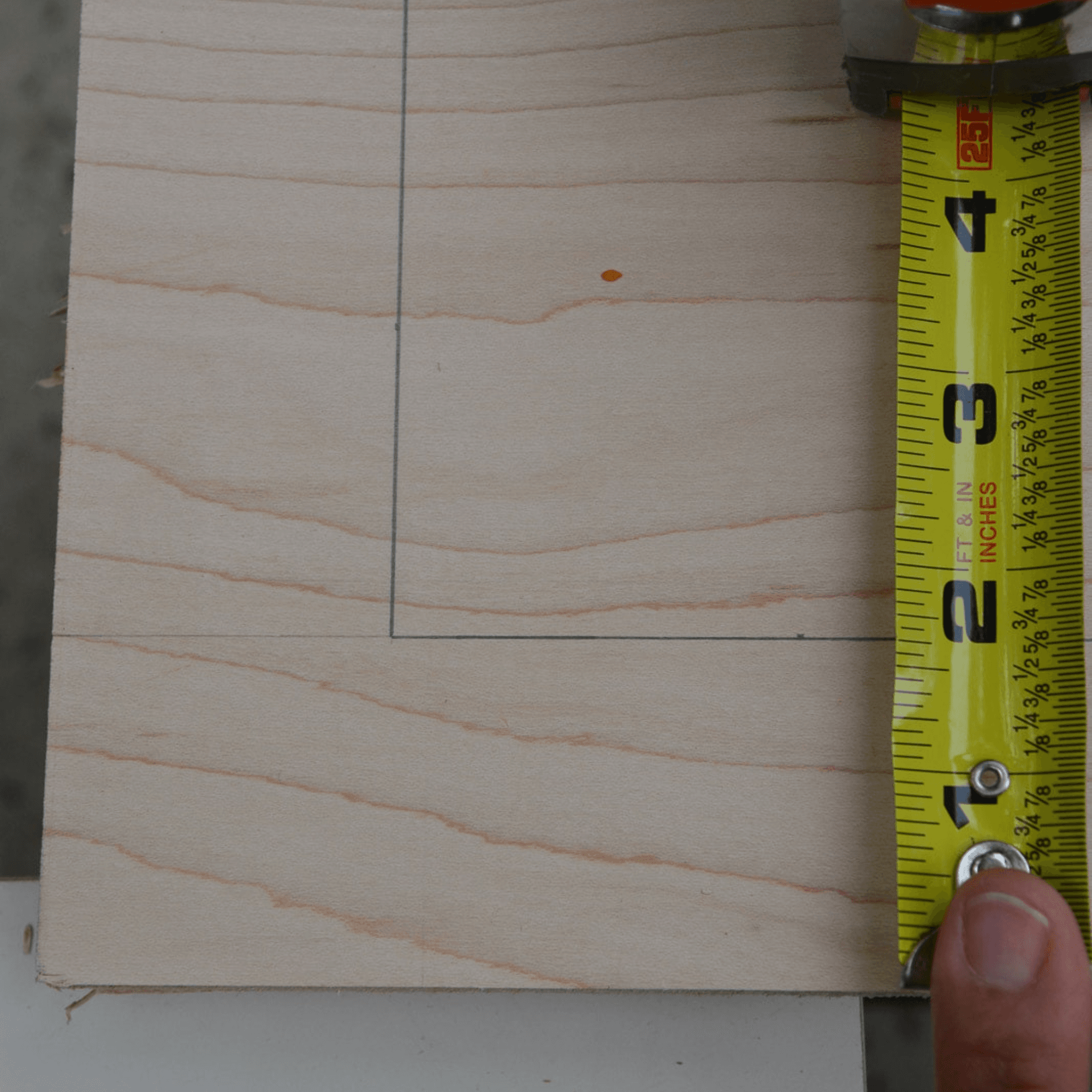 Tape measure positioned along a piece of wood marked with pencil lines to measure and outline a rectangular cut or placement area.