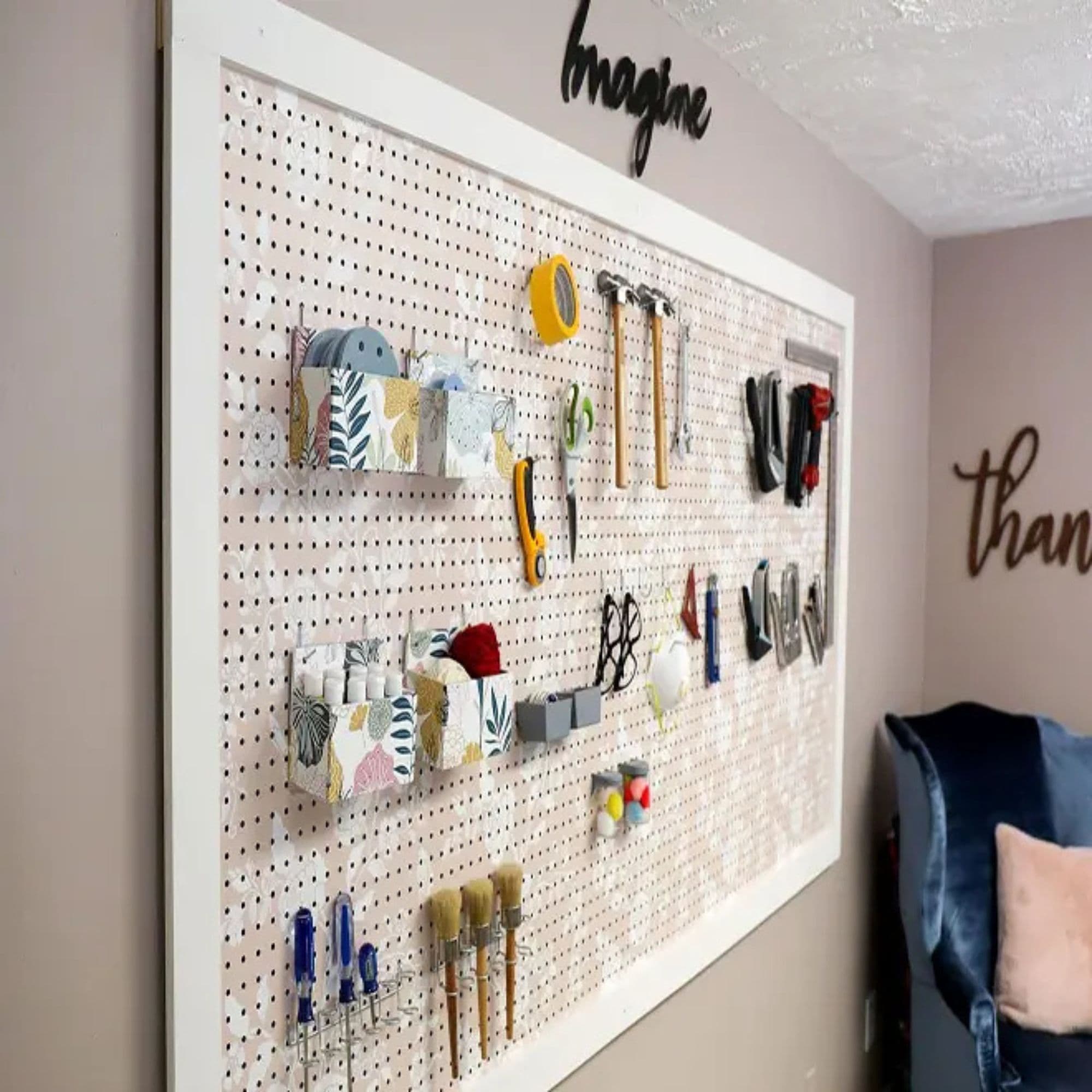 Framed white pegboard mounted on a wall, neatly organizing hand tools, craft supplies, tape, scissors, brushes, and storage containers.