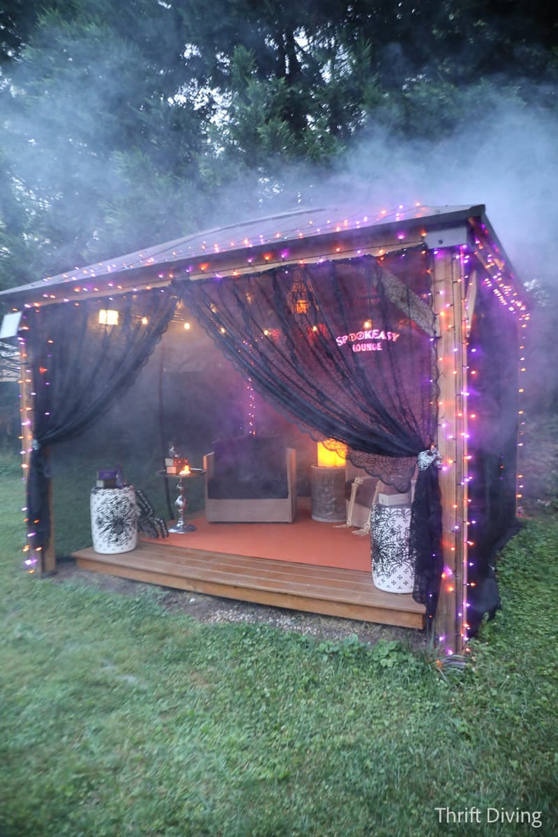 Photo of a porch covered in Halloween lights and decorations in Serena's backyard. The gazebo is covered in smoke and there is a sign in the back of it that reads 'Spookeasy Lounge'/