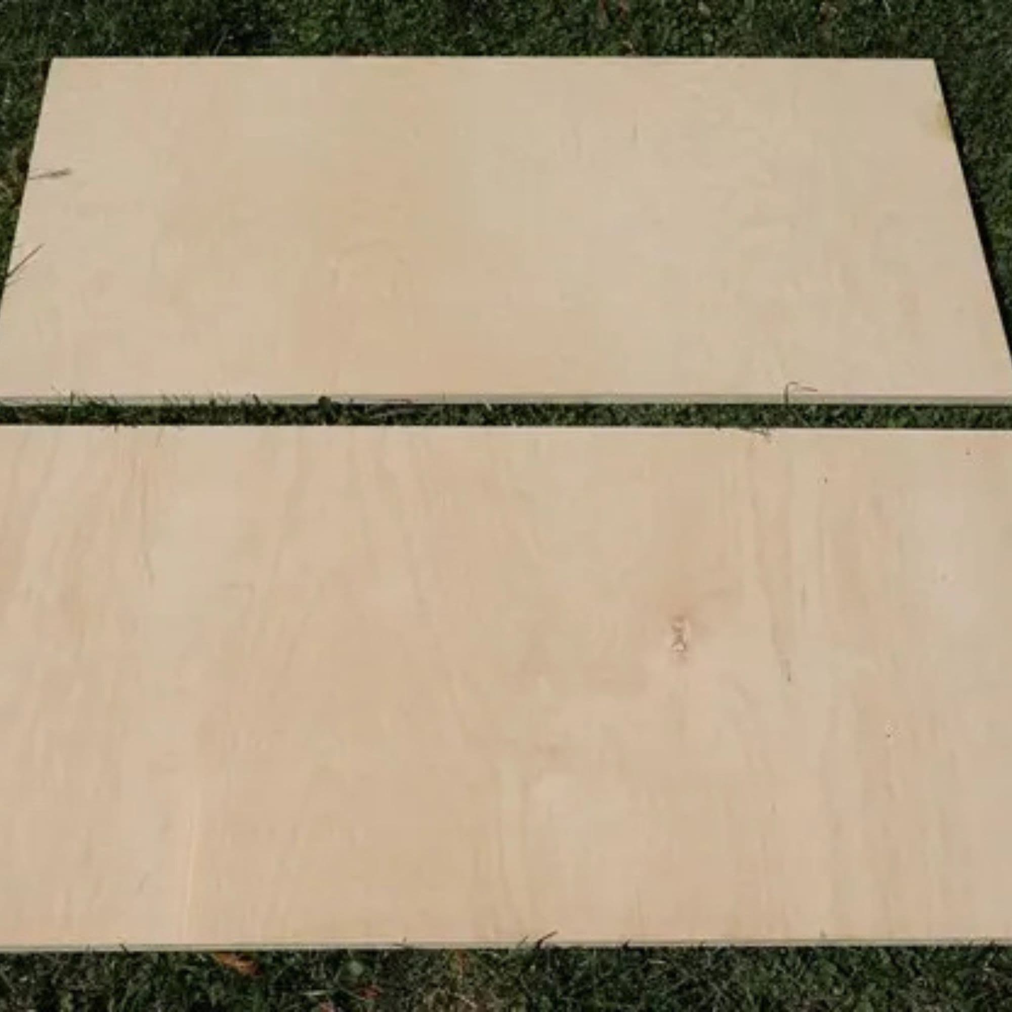 Two rectangular plywood boards laid in the grass, cut in half lengthwise
