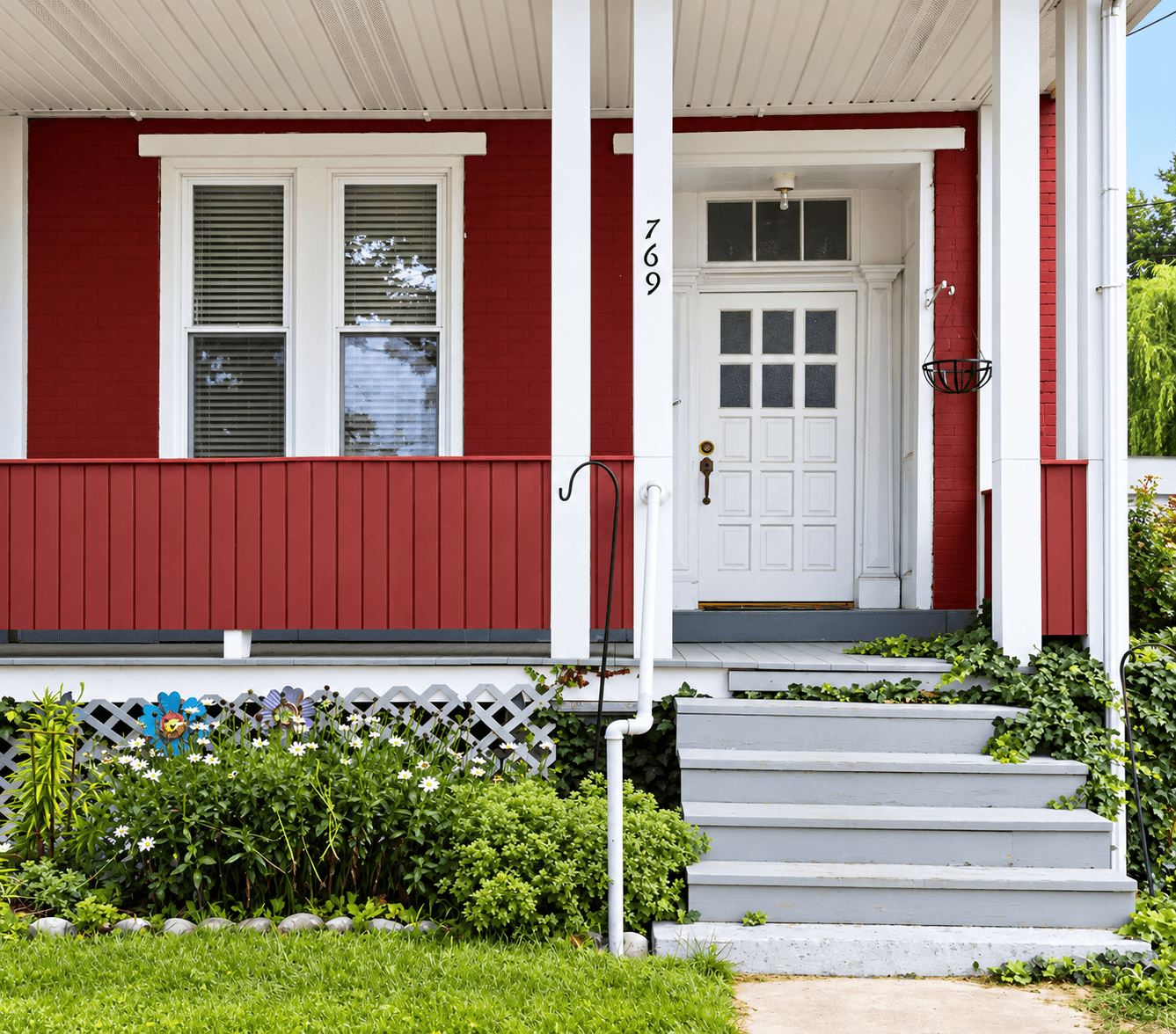 Front porch of a red house with white trim, gray steps, a white entry door, and a landscaped garden with green plants and flowers.