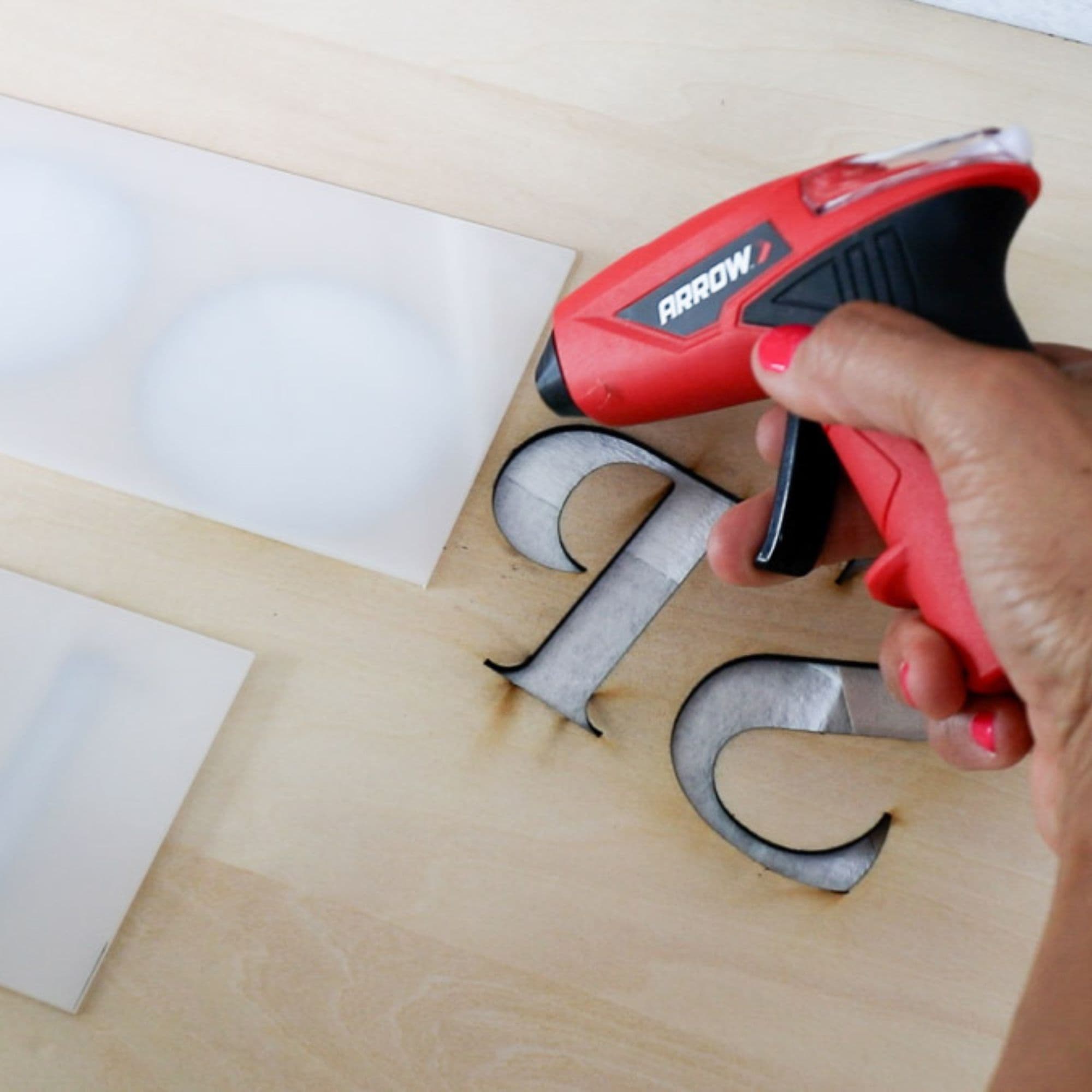 Serena glues frosted acrylic onto her wooden sign using a glue gun.