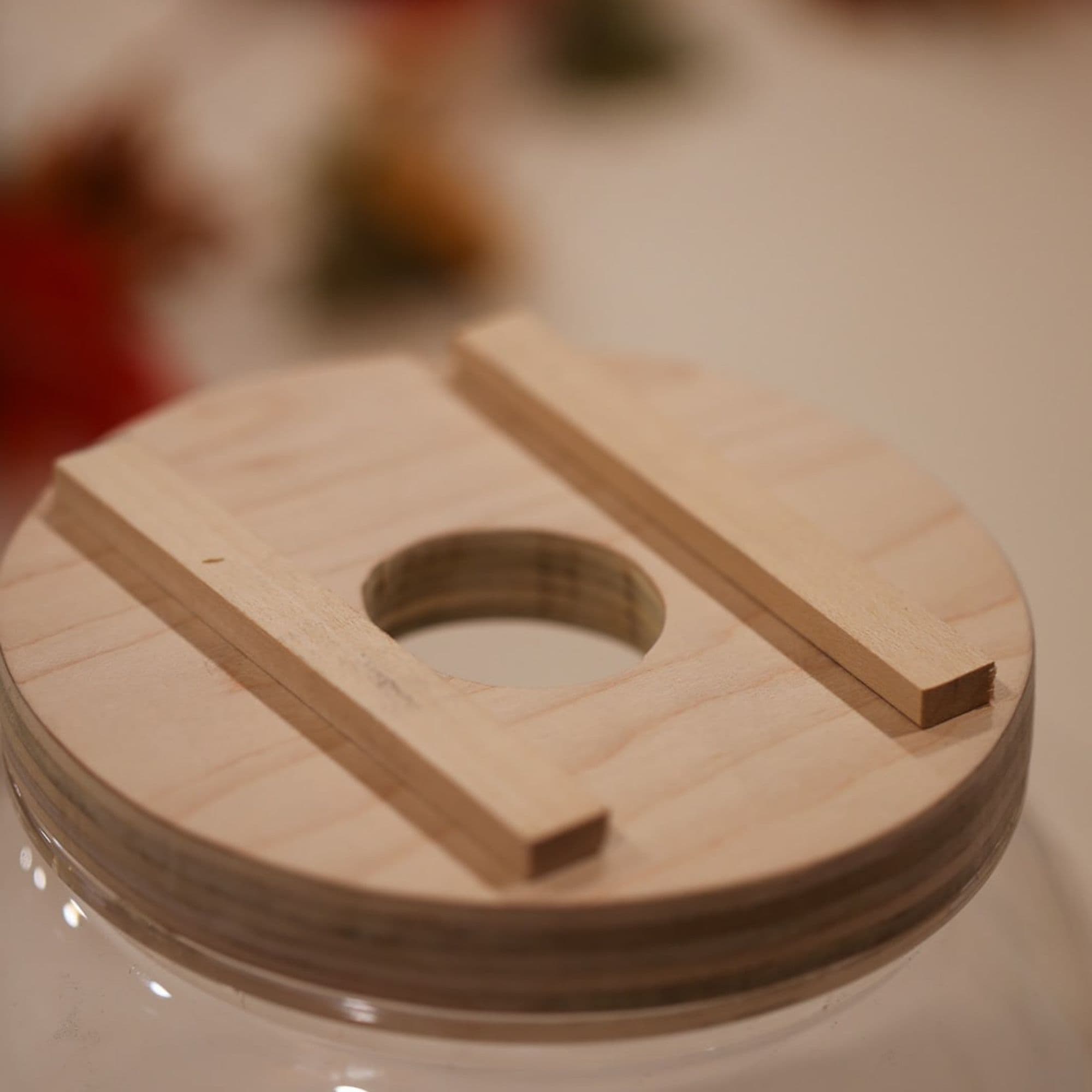Circular wooden lid with a center hole and two narrow wood strips attached across the top for a DIY candy dispenser project.