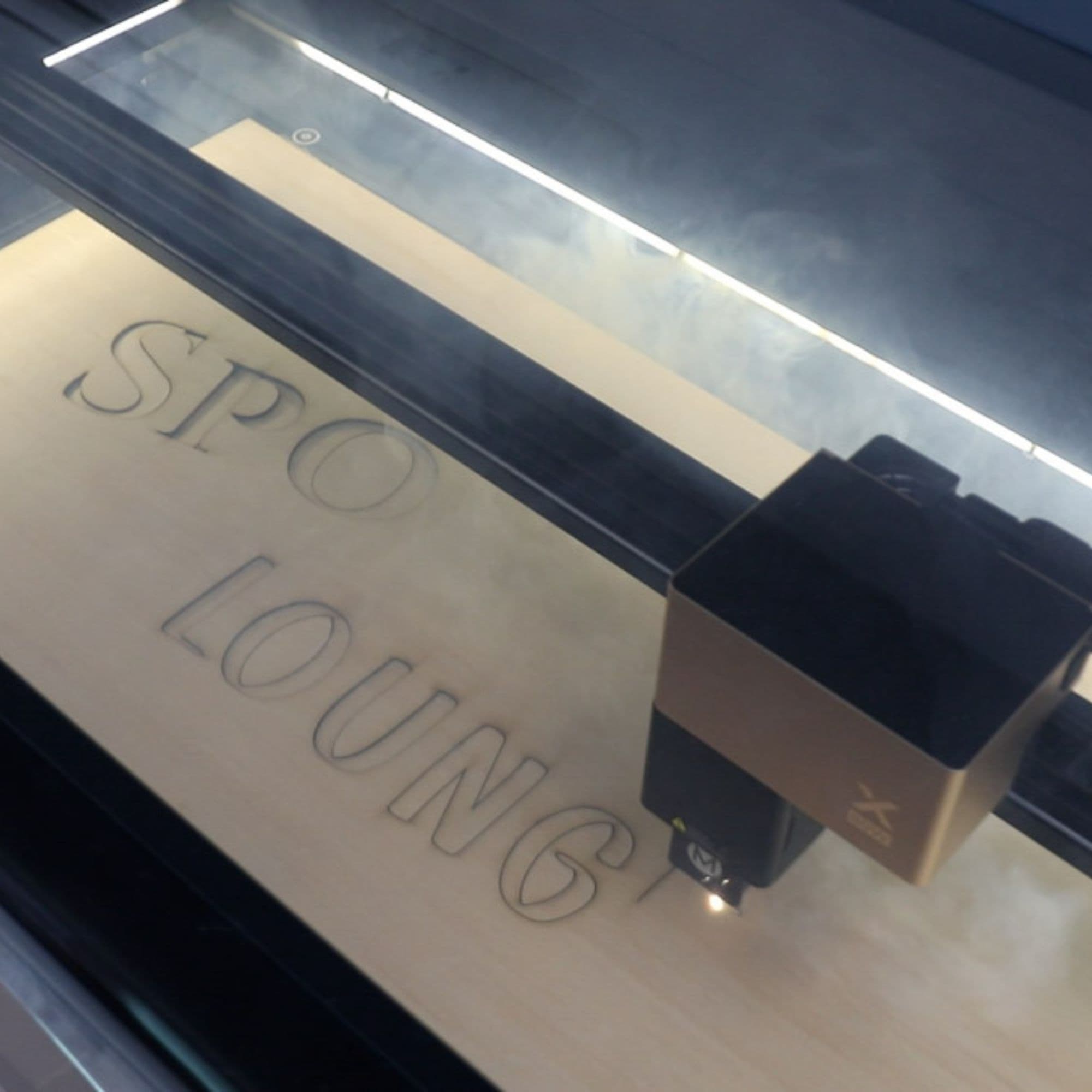 Serena is using a laser cut machine to cut letters into wood. The letters read 'Spookeasy Lounge'.