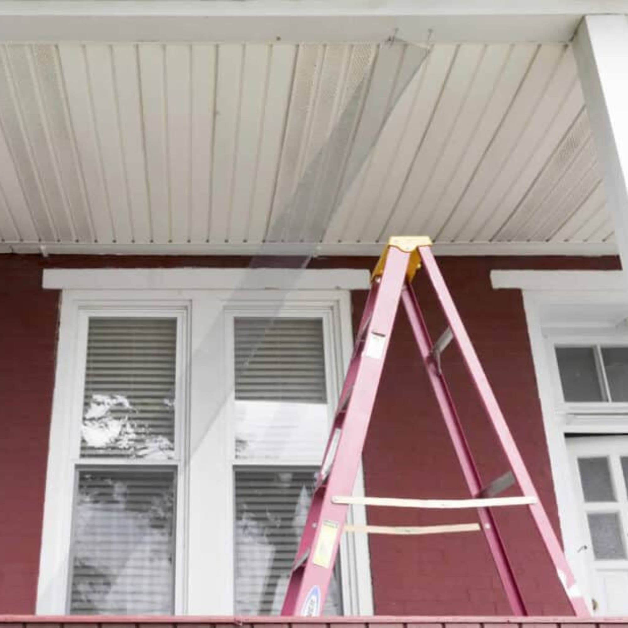 A ladder on the porch of a red house.