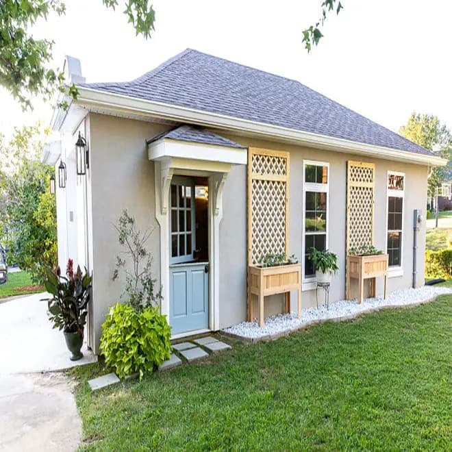 Finished exterior of a small home featuring two wooden planter boxes with lattice trellises, greenery, and landscaped surroundings.