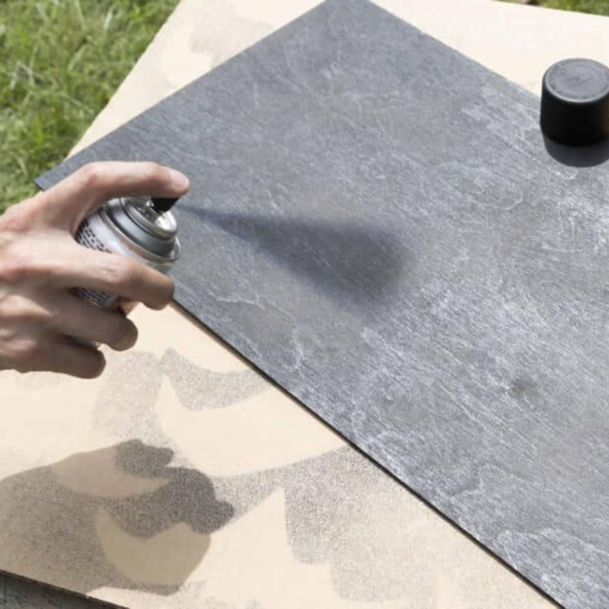 A person spray paints a piece of plywood black.