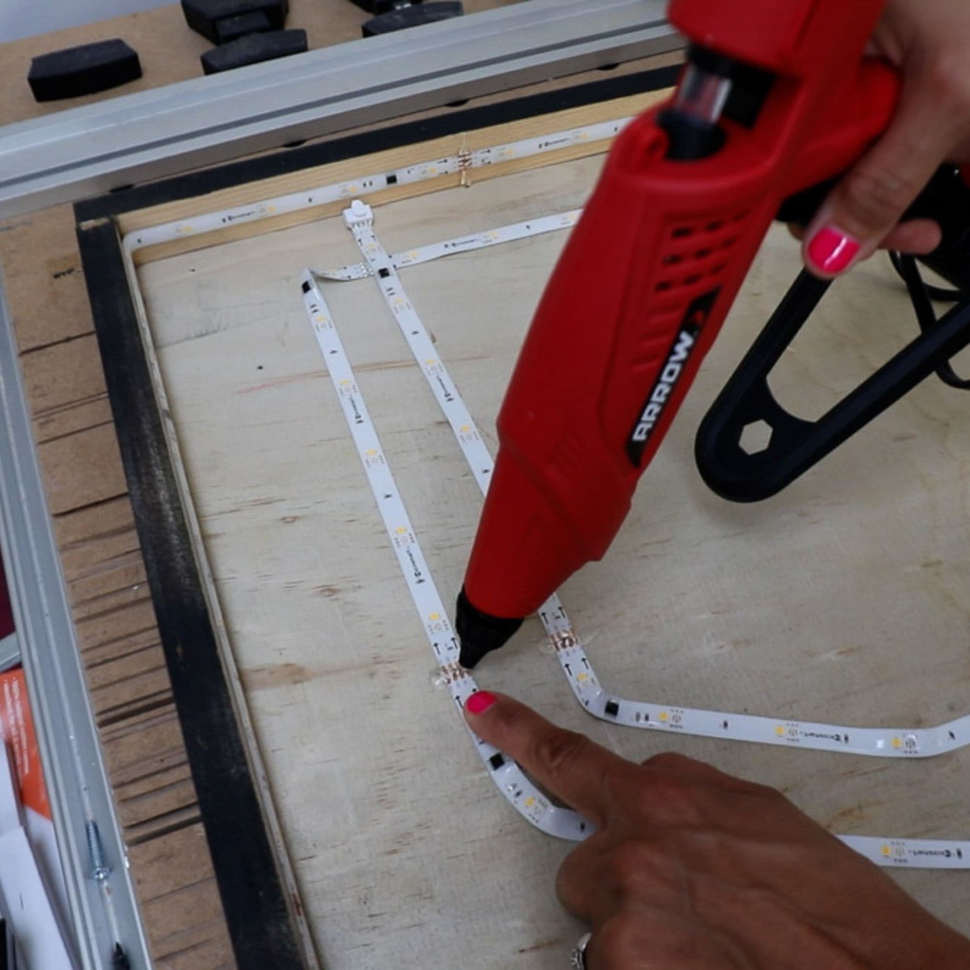 Serena glues an LED strip to the back of her sign using a glue gun.