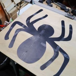 Serena tapes her cut out spider onto a piece of wood.
